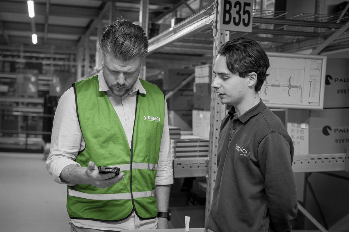 Een consultant en medewerker bekijken samen een handterminal in het magazijn.