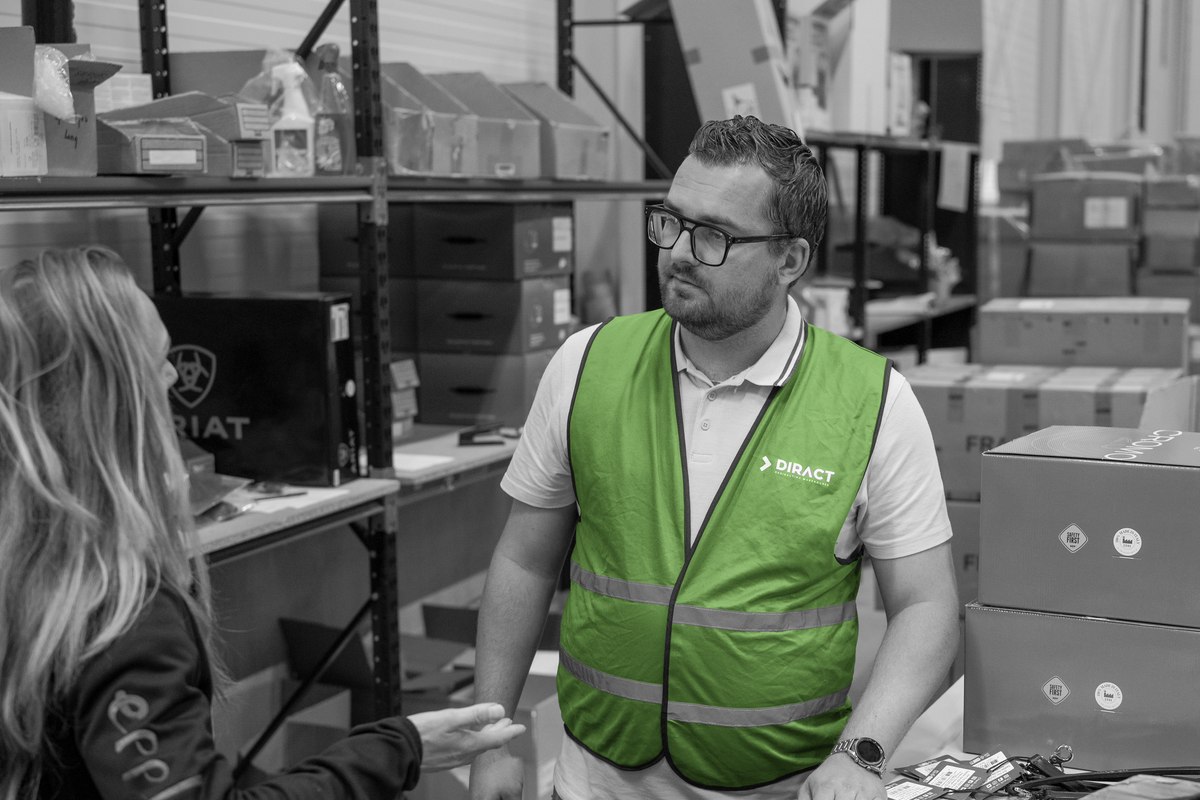 Een consultant bespreekt het magazijnproces met een medewerker tussen de stellingen.
