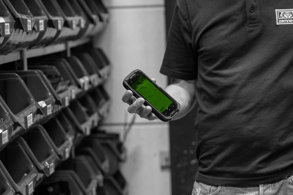 Een handterminal bij blauwe pickbakken in het magazijn.