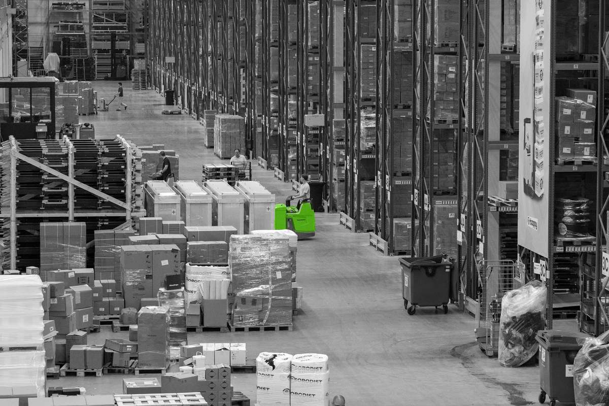 Een lange magazijngang met palletstellingen en goederen.