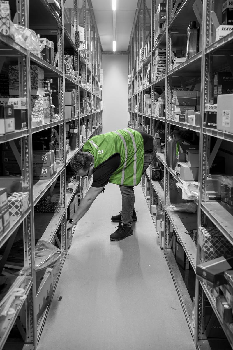 Een medewerker verzamelt onderdelen bij de stellingen in een magazijngang.