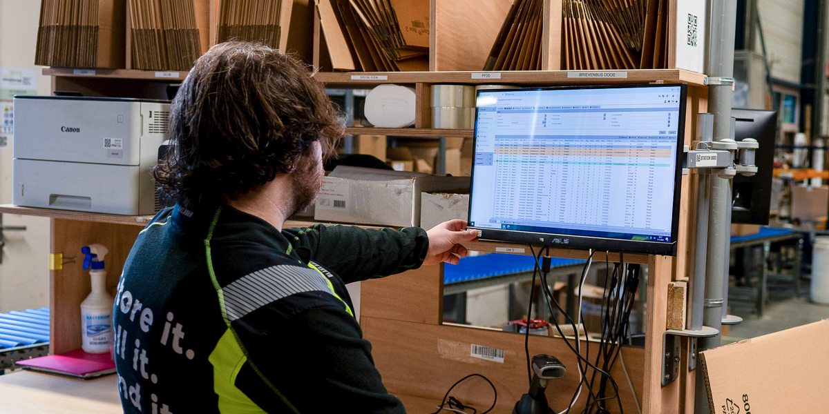 Medewerker bij een werkplek in het magazijn met het WMS-scherm voor zich